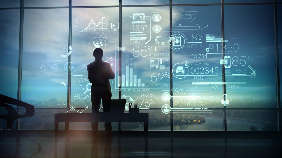 A silhouette of a man stands on the background of large office windows and views a hologram of infographic with data.